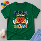 Jesus Holds My Heart Christian kids shirt in green featuring a smiling heart with faith-inspired typography
