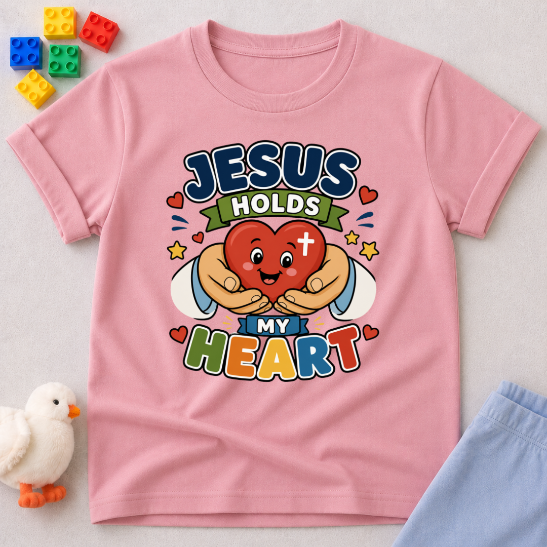 Jesus Holds My Heart Christian kids shirt in pink featuring a smiling heart with faith-inspired typography
