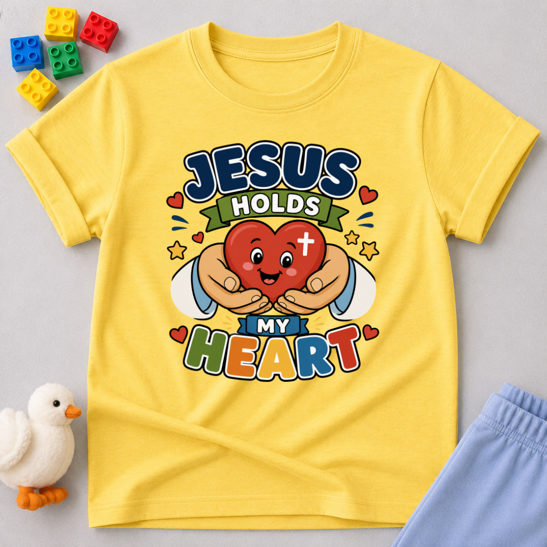 Jesus Holds My Heart Christian kids shirt in yellow featuring a smiling heart with faith-inspired typography

