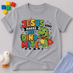 Jesus Makes Me Dino-Mite Christian kids shirt in gray featuring a smiling dinosaur with a cape
