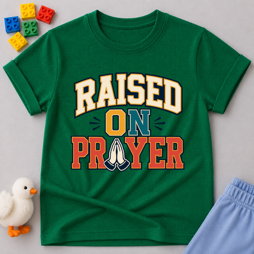 Raised on Prayer Christian kids shirt in green featuring bold typography and praying hands
