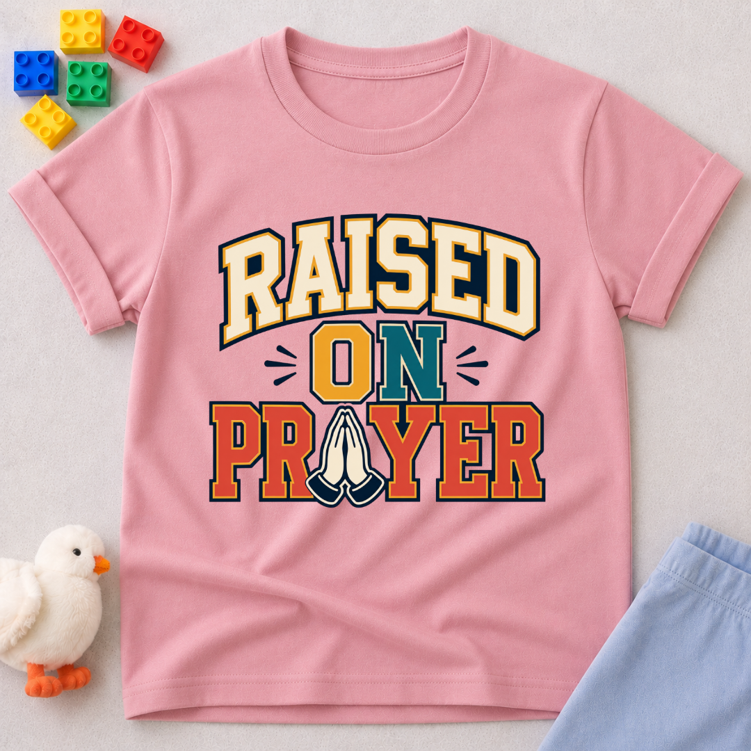 Raised on Prayer Christian kids shirt in pink featuring bold typography and praying hands
