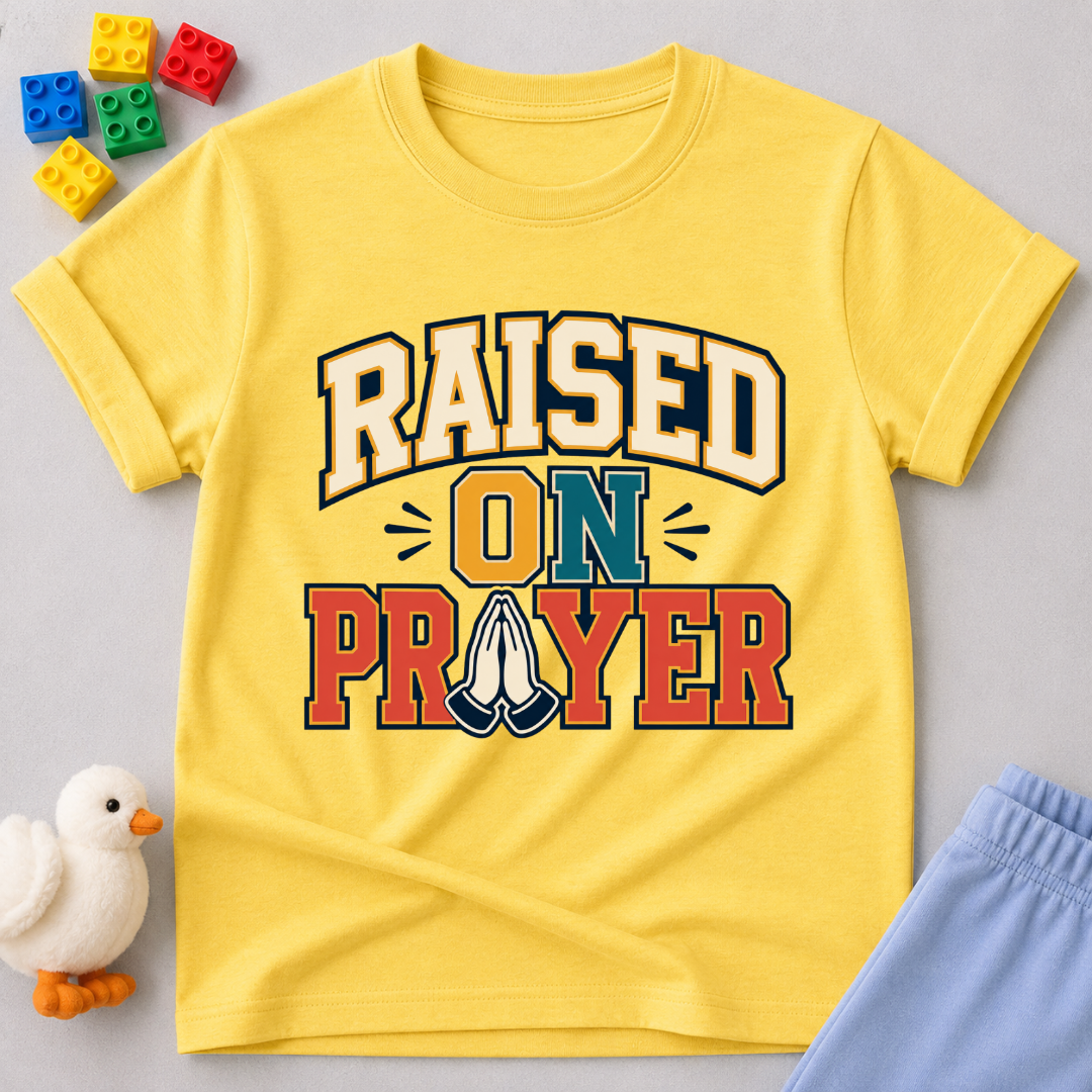 Raised on Prayer Christian kids shirt in yellow featuring bold typography and praying hands
